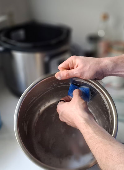 Hands scrubbing inner pot bottom with non-abrasive sponge